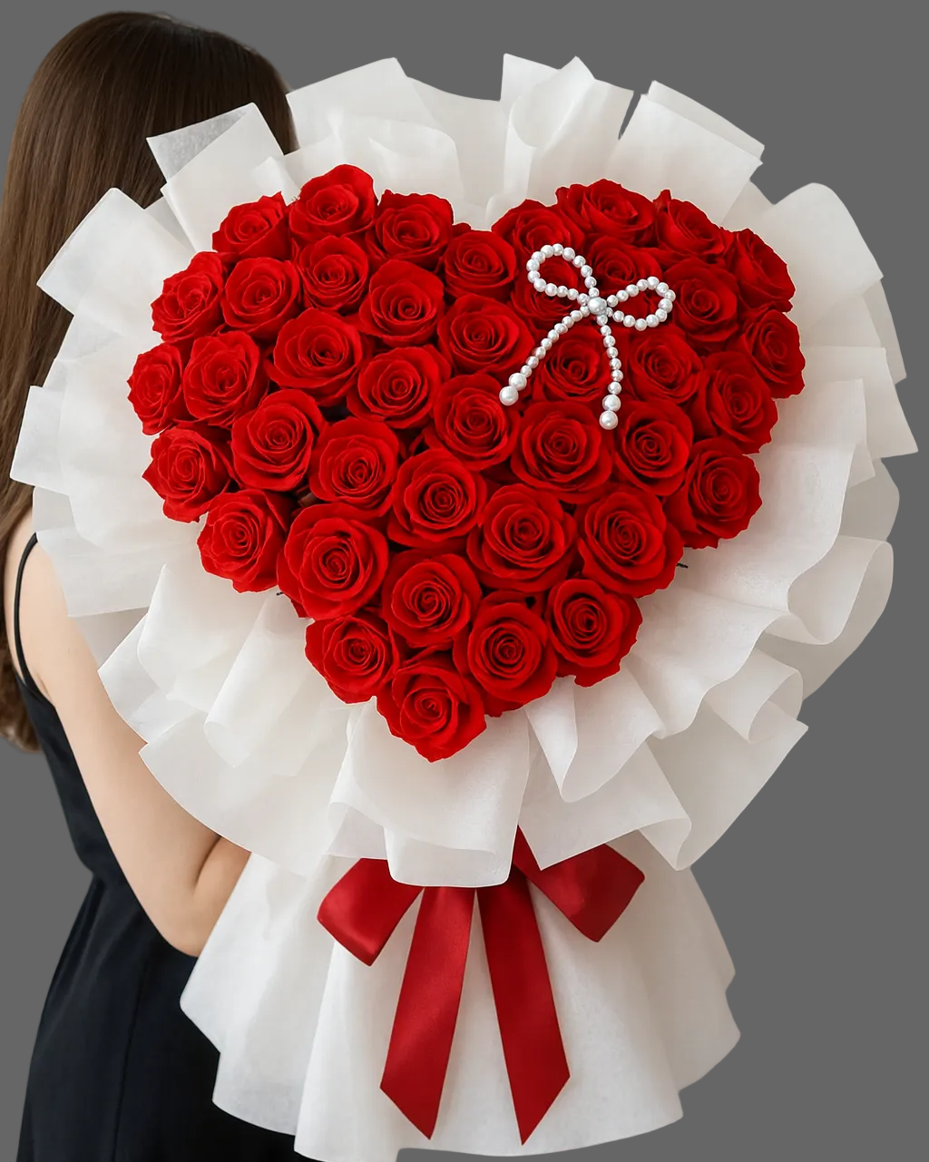 Heart-shaped bouquet of premium red roses wrapped in white paper, held by a woman.