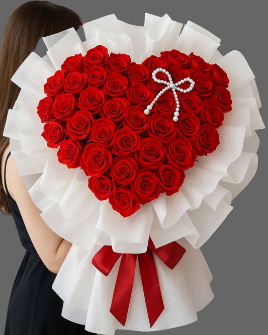 Heart-shaped bouquet of premium red roses wrapped in white paper, held by a woman.