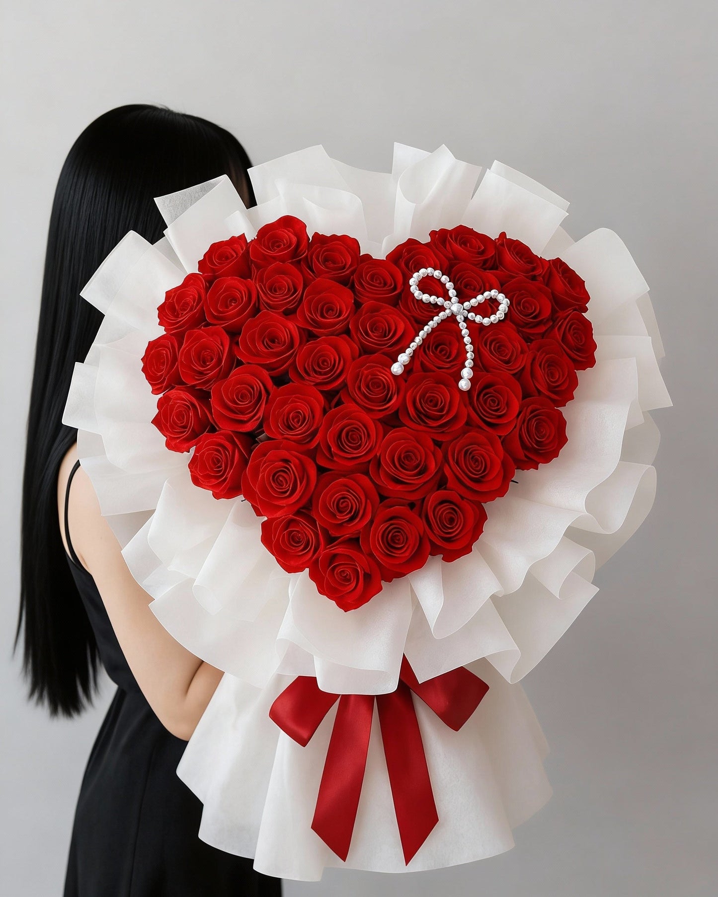 Heart-shaped bouquet of premium red roses wrapped in white paper, held by a woman.