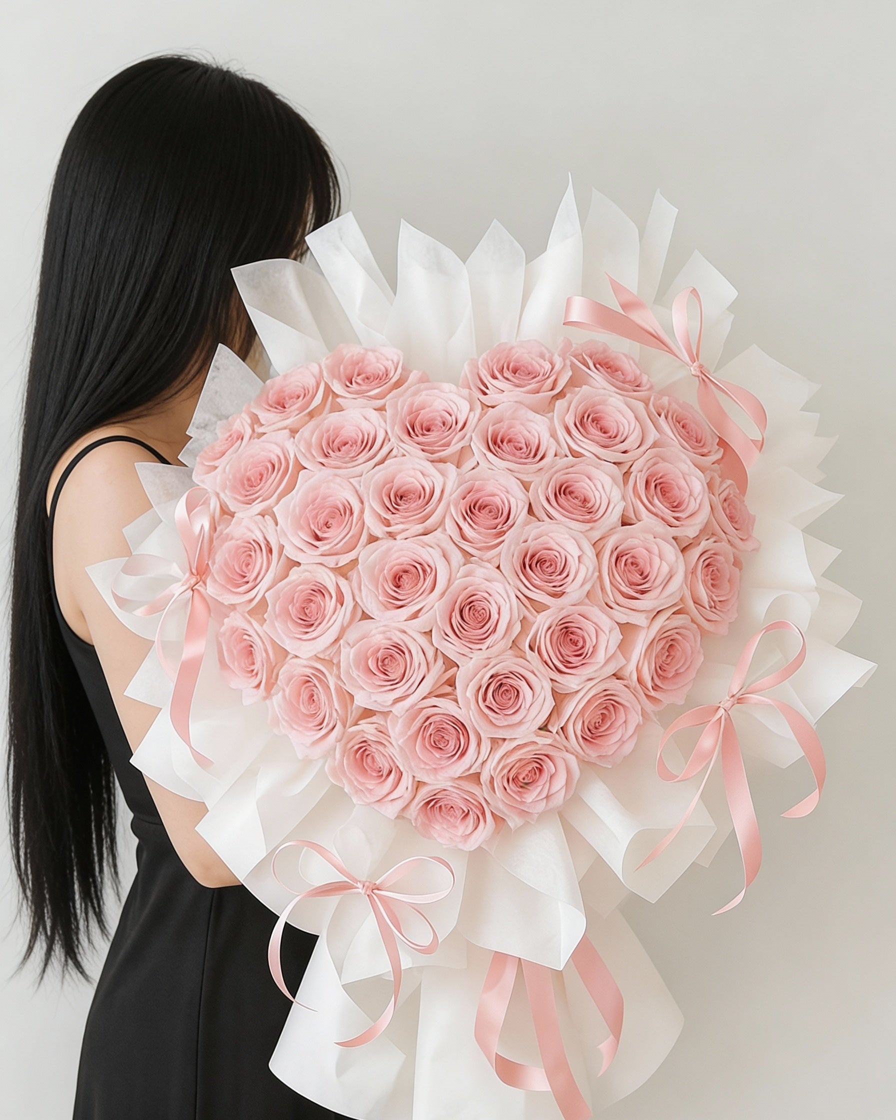 Person holding a large heart-shaped bouquet of pink roses against a plain background